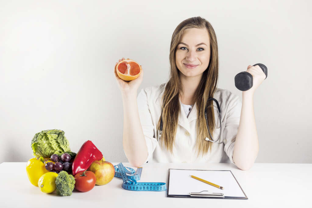 female-dietician-holding-grapefruit-dumbbell-clinic