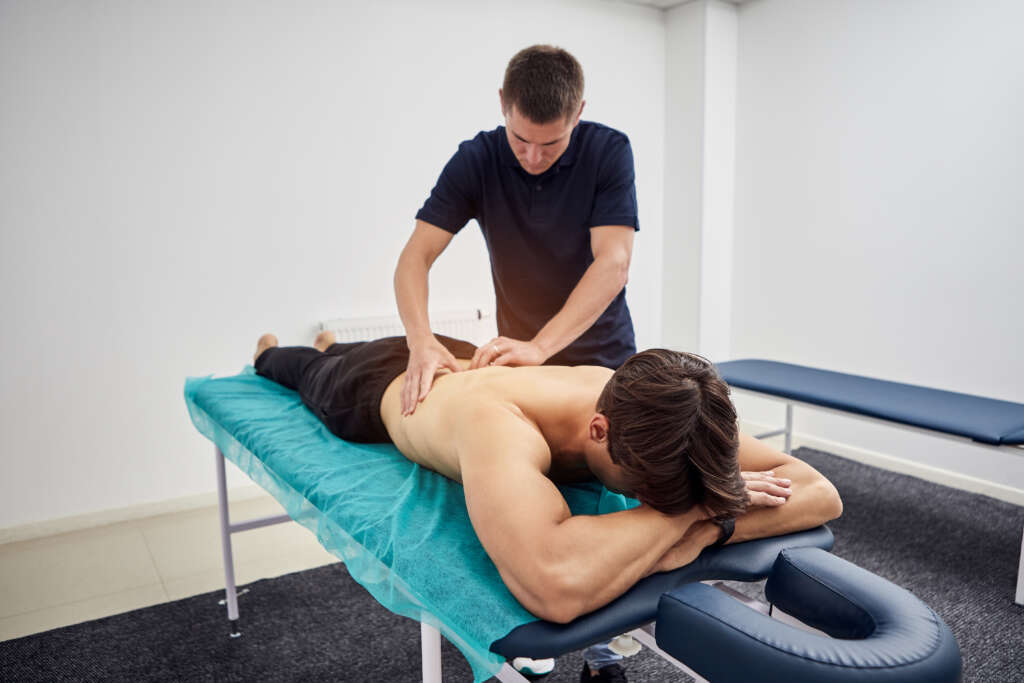 Physiotherapist massaging a male patient sportsman with damaged muscles in kinesio clinic. Treatment of sports injuries.